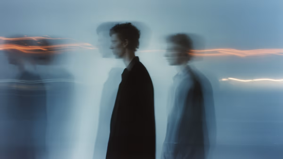 Blurred silhouettes of two men walking with streaks of orange and white light against a blue background.